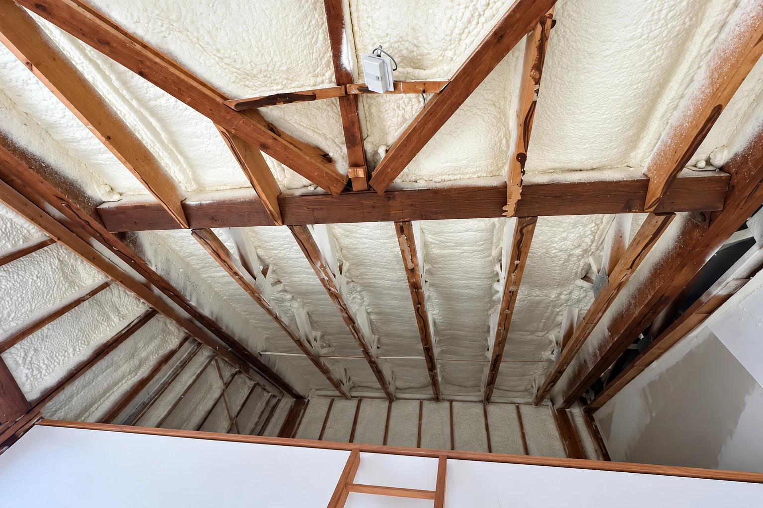 White spray foam seals the roof underside and fills spaces between exposed wooden rafters.