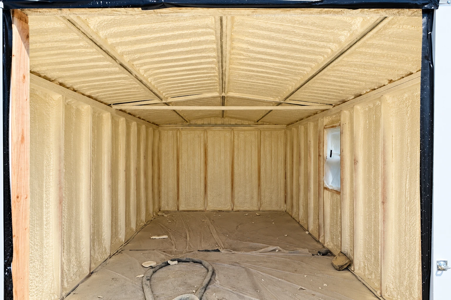 Small framed room coated with tan closed-cell spray foam across its walls and ceiling.