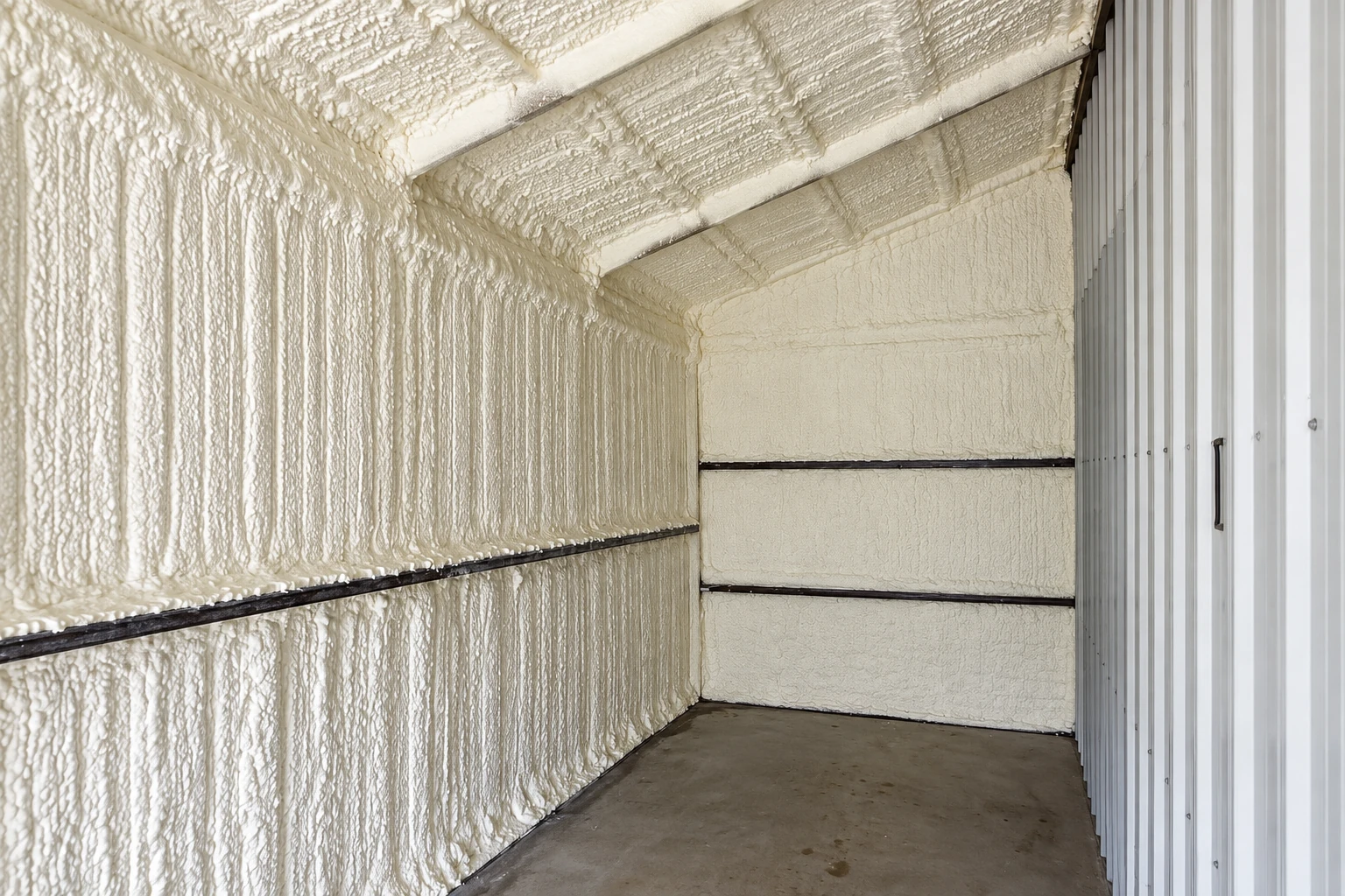 A metal-walled commercial space has thick white spray foam covering its ceiling and walls.