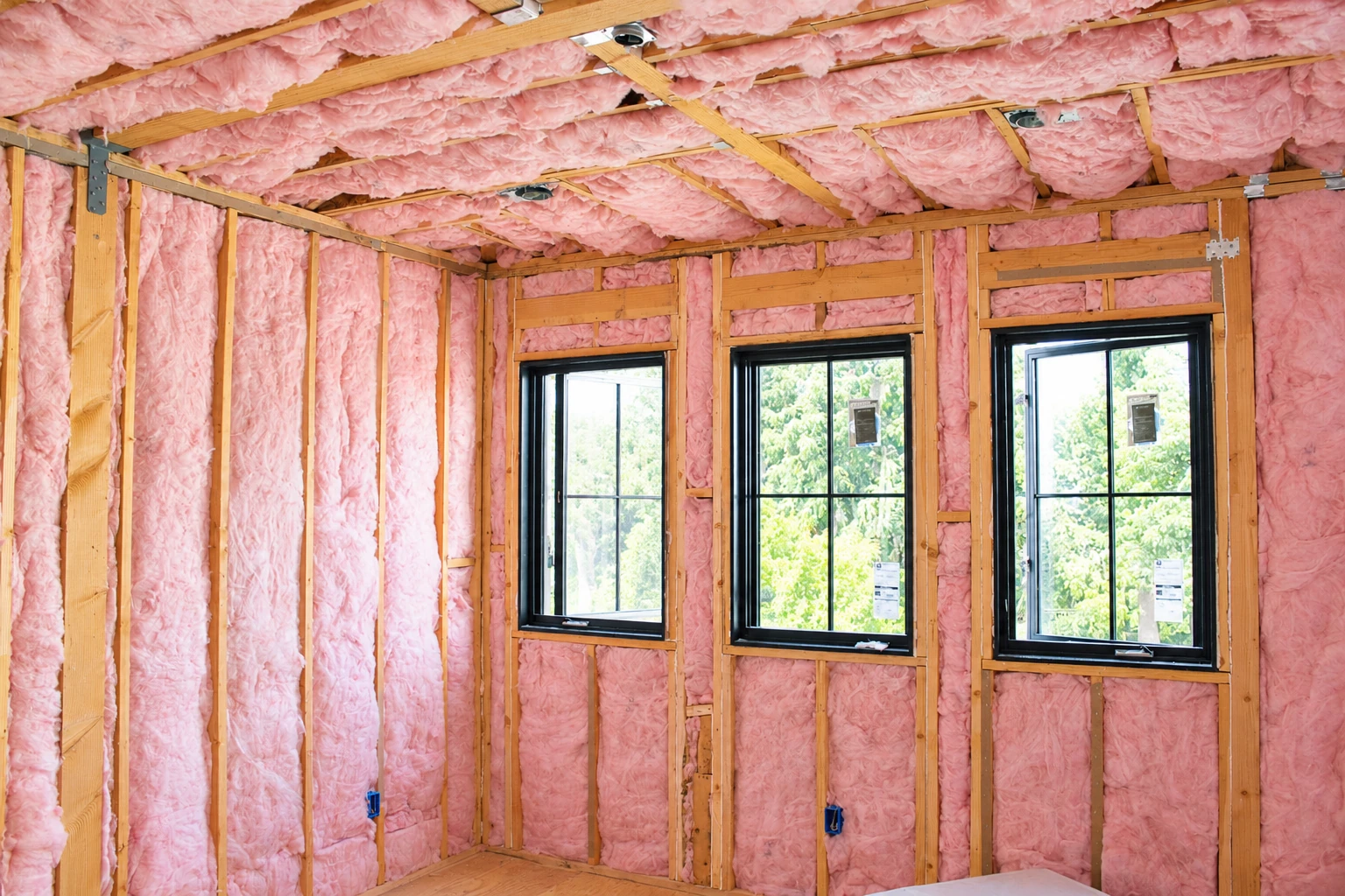 Pink fiberglass insulation fills the walls and ceiling between the framing in an unfinished room.